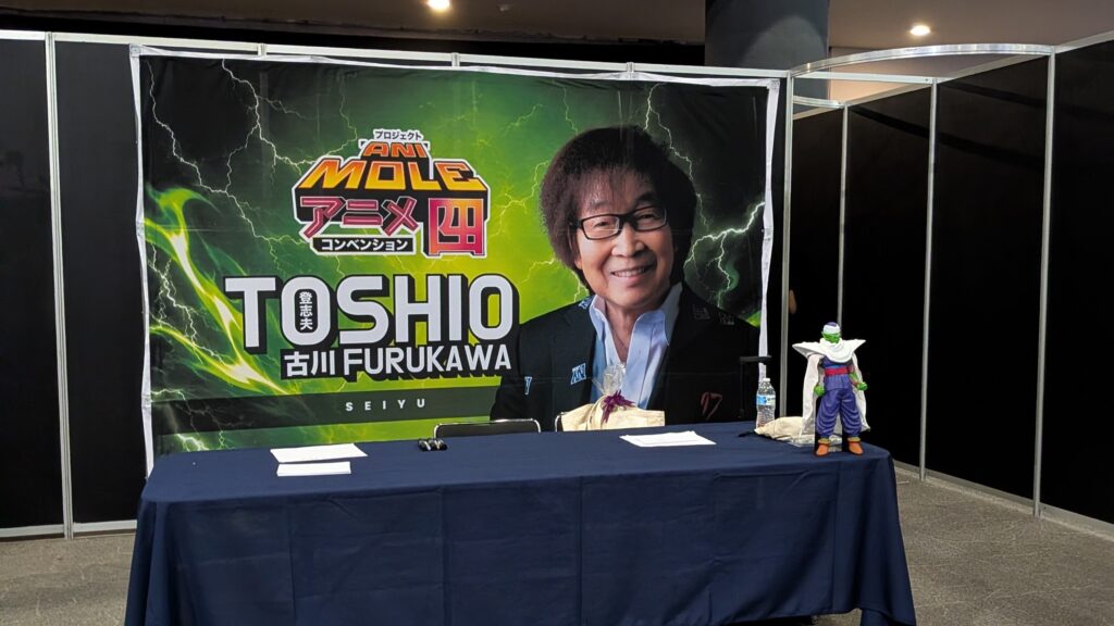 アニモレ会場のゲスト登壇ブース。声優・古川登志夫氏のサイン会用バックパネルと、隣に飾られたピッコロのフィギュア